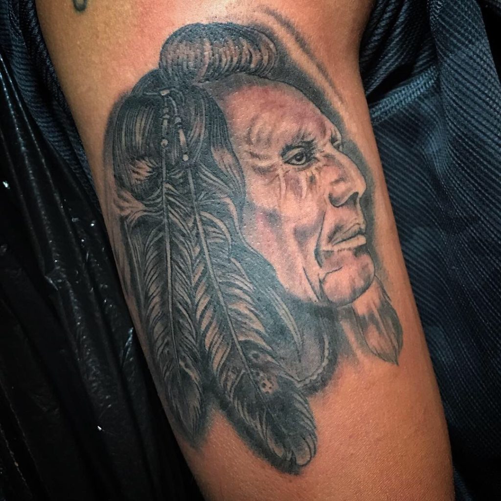 Black-and-grey portrait and feather tattoo on the upper arm.