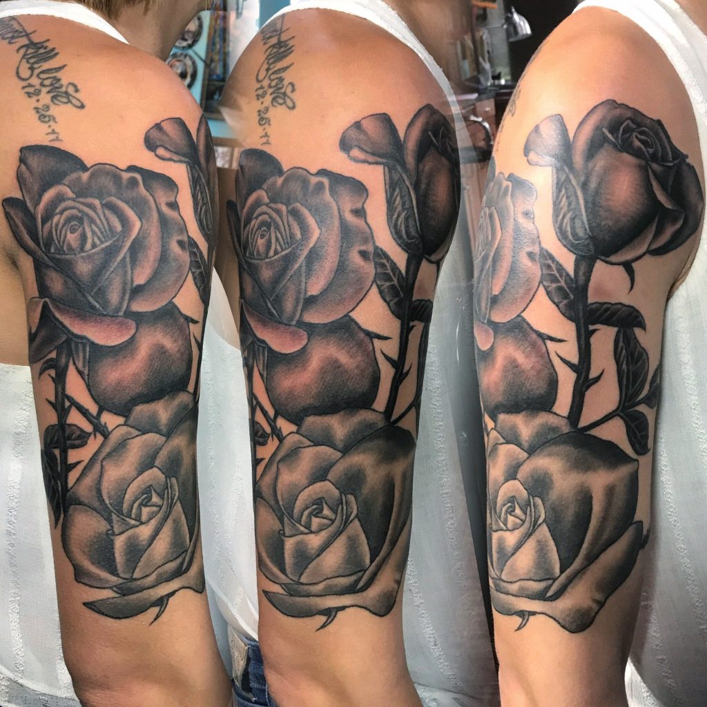 Black-and-grey rose tattoos with stems and script on the legs.