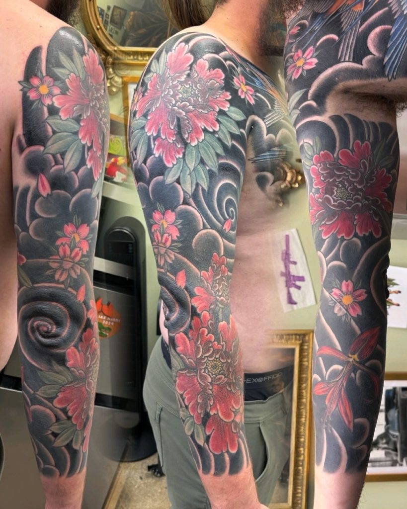Dark botanical leg tattoos with pink blossoms.