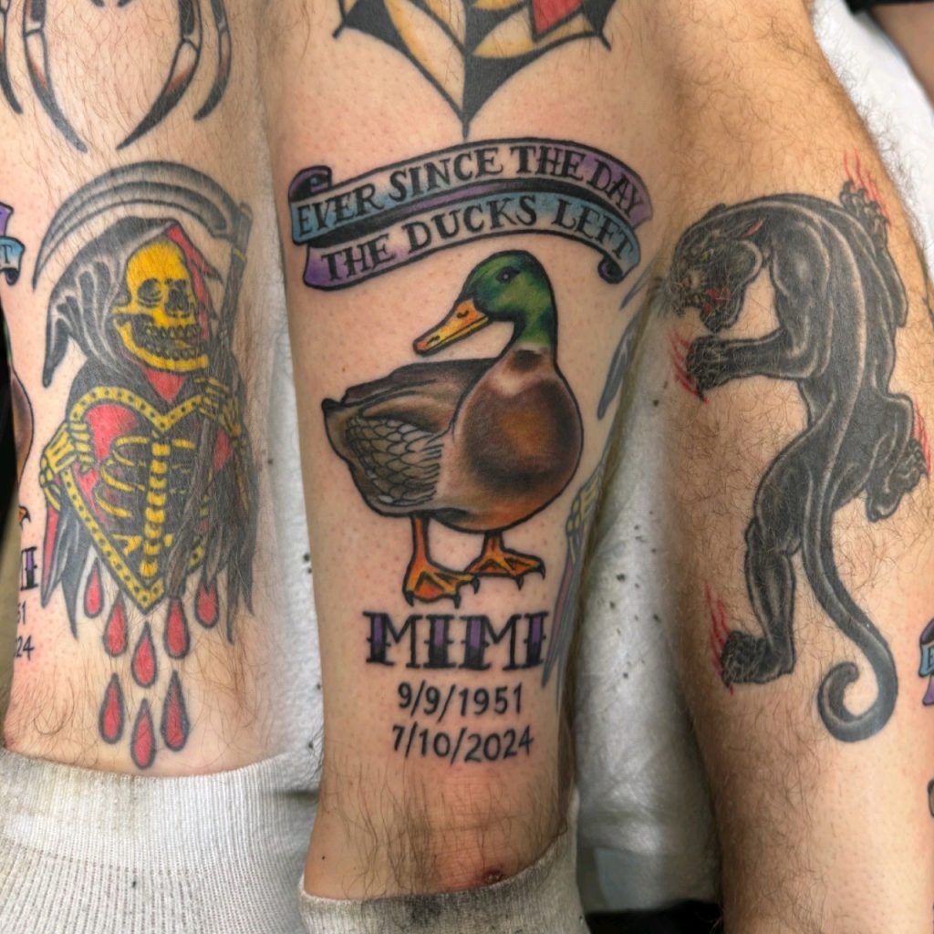 Lower-leg tattoos depicting a skeleton, duck, and dark-haired mermaid.