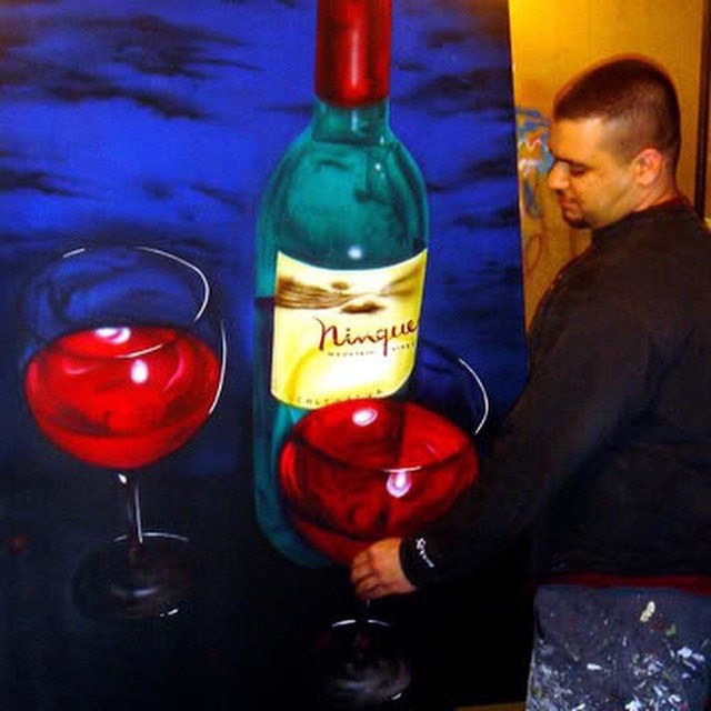 Painting of a wine bottle, two red wine glasses, and a figure.