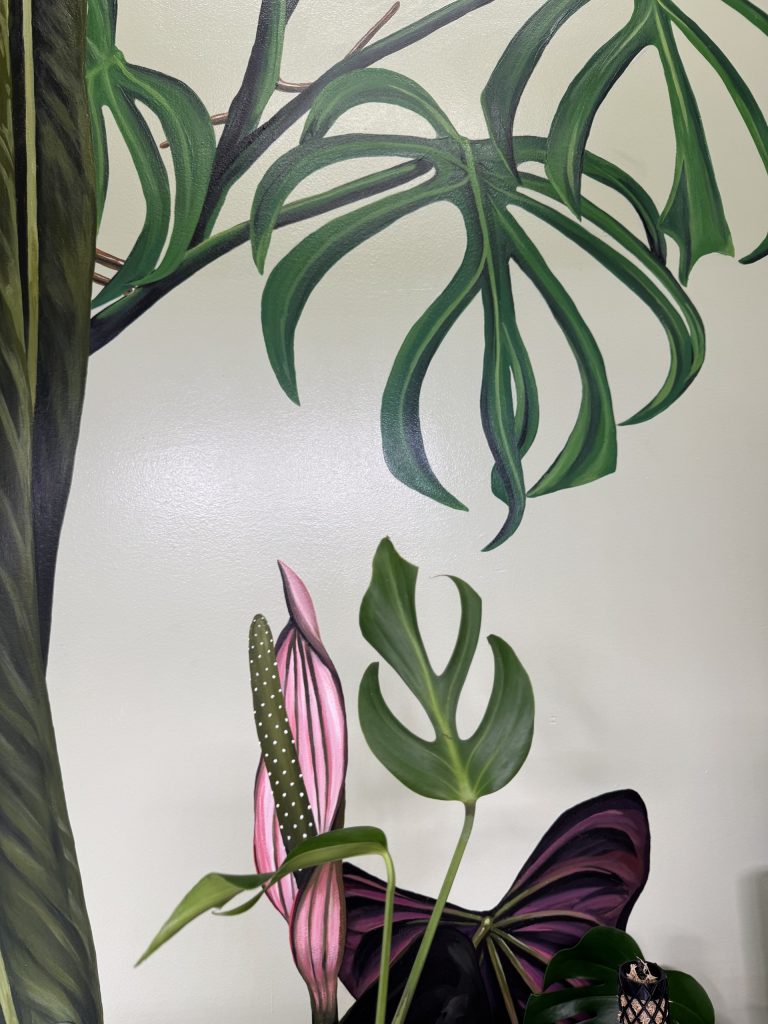 Close-up botanical mural with broad green leaves and a pink flower.